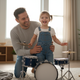 A father and his laughing young child playing a drum together at home